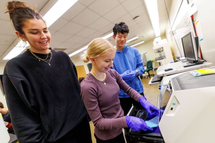 Ivy Isenberg (from left) Raegan Mulliner, and Andy Nguyen place their gel containing DNA into a GelDocGo machine during Genetics, Molecular and Cellular Biology Lab in Manter Hall.