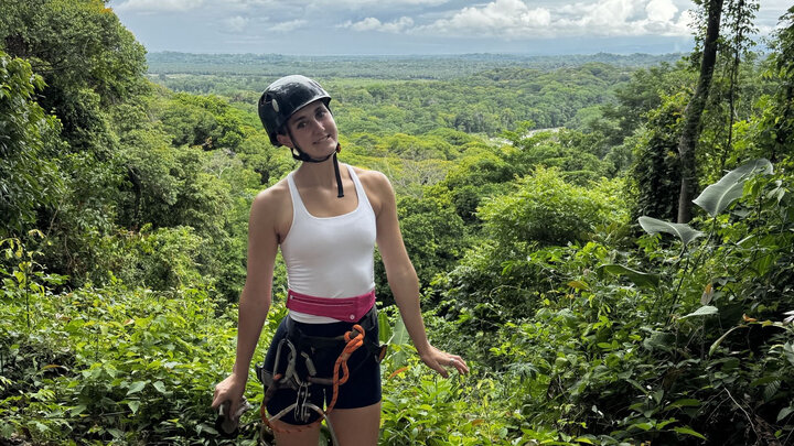A young woman stands with a forest in the background.